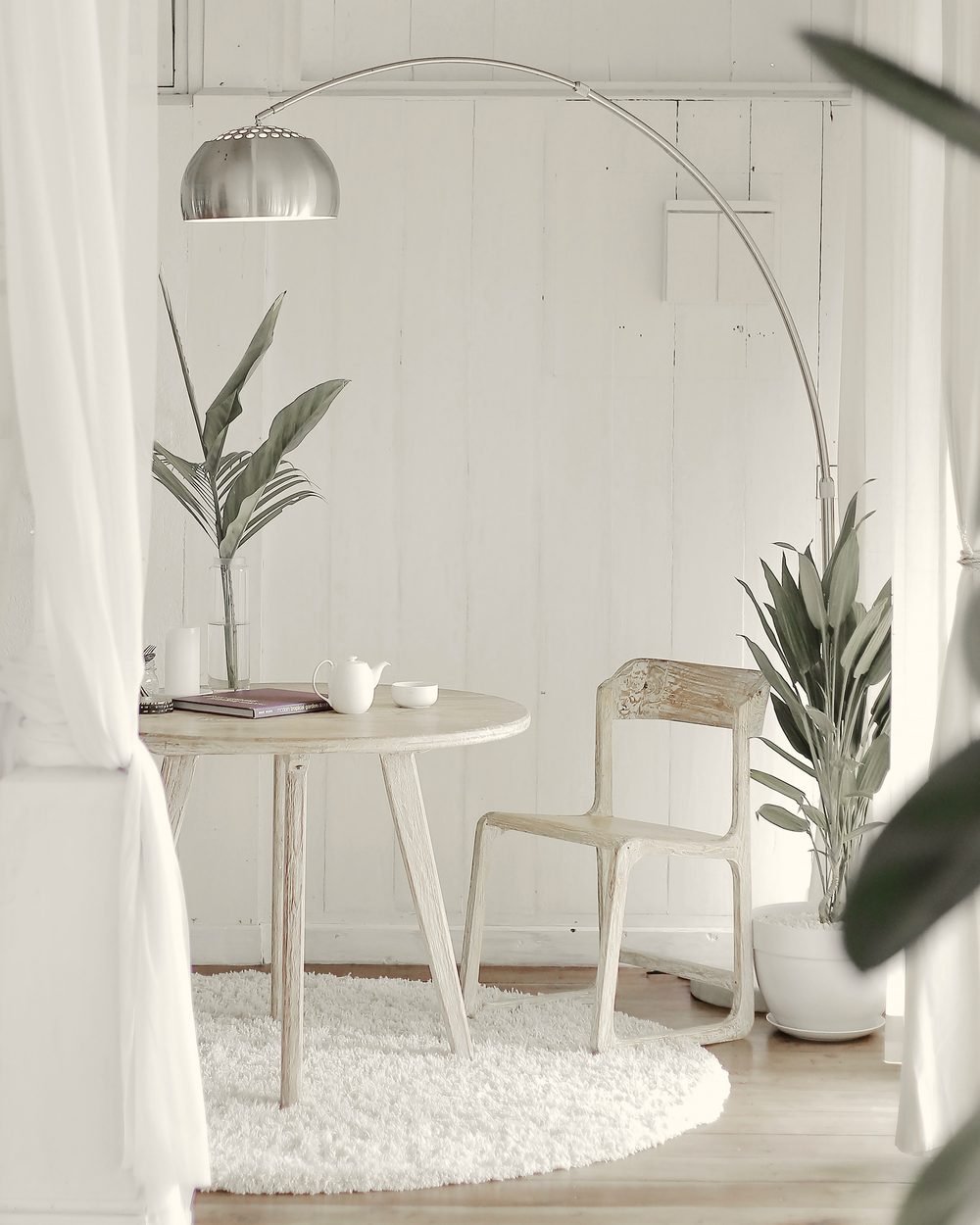 Round pale wood dining table and chair in a quiet white room with linen curtains